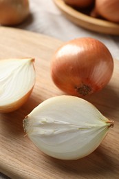 Whole and cut onions on wooden board, closeup