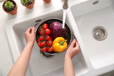 Photo of Woman washing fresh vegetables in kitchen sink, top view