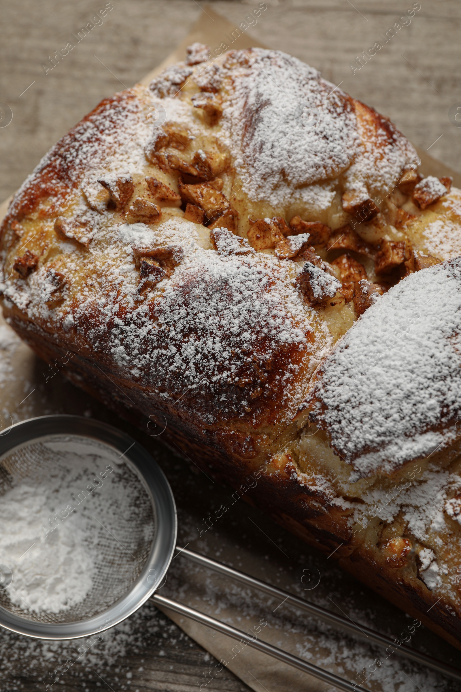 Photo of Delicious yeast dough cake and strainer with powdered sugar on wooden table, closeup