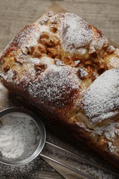 Delicious yeast dough cake and strainer with powdered sugar on wooden table, closeup