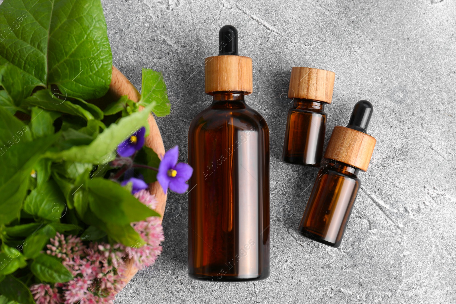 Photo of Glass bottles of essential oil and bowl with different wildflowers on light grey table, flat lay