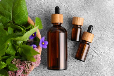 Photo of Glass bottles of essential oil and bowl with different wildflowers on light grey table, flat lay