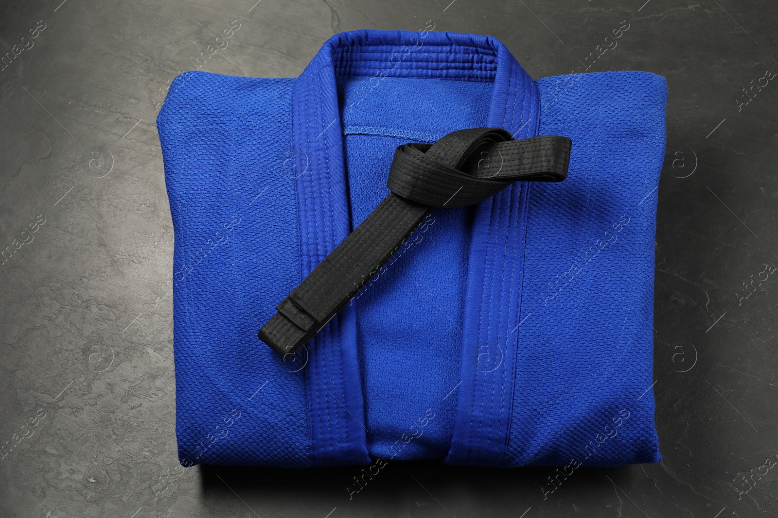 Photo of Black karate belt and blue kimono on gray background, top view