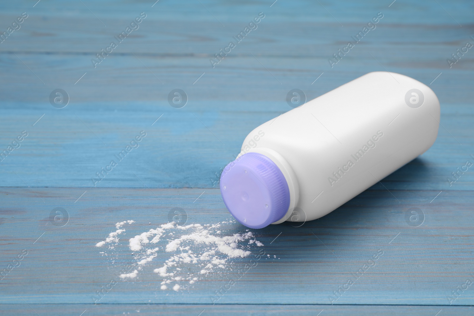 Photo of Bottle and scattered baby powder on light blue wooden table. Space for text