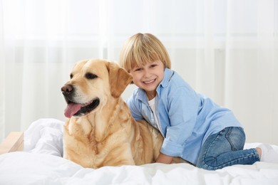 Photo of Cute little child with Golden Retriever on bed at home. Adorable pet