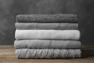 Photo of Stack of warm clothes on wooden table against grey background. Autumn season