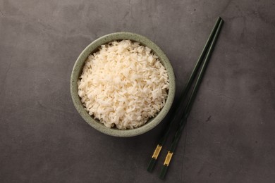 Delicious rice in bowl and chopsticks on grey table, flat lay