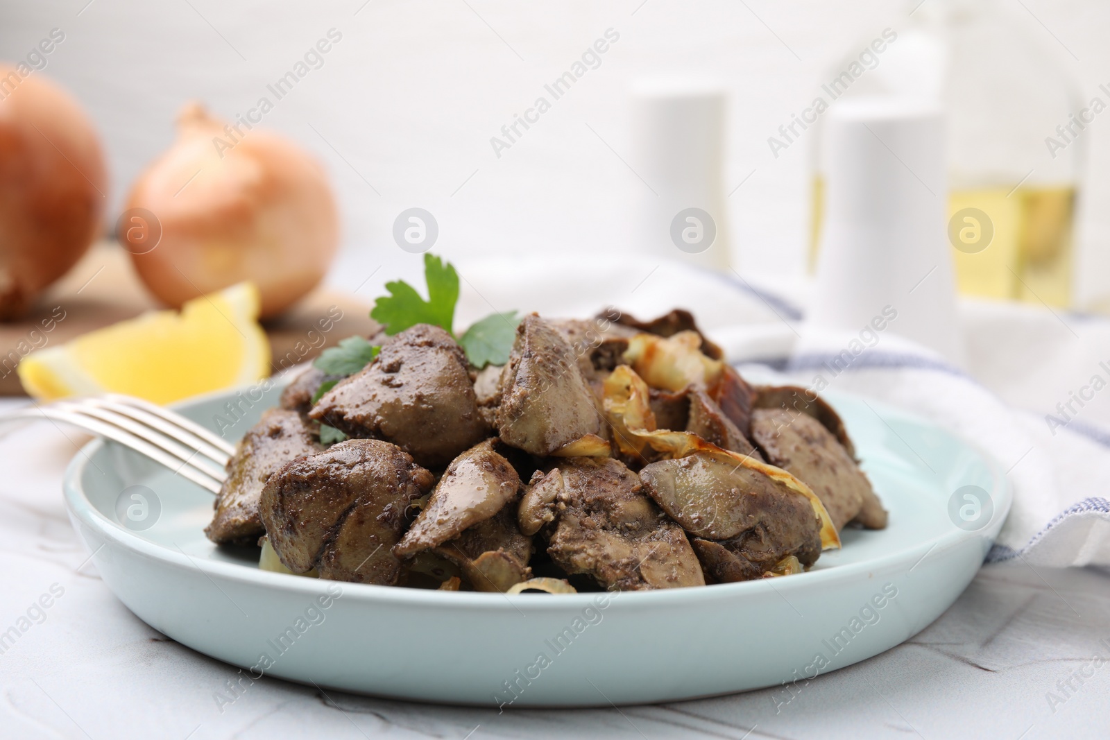 Photo of Tasty fried chicken liver with onion and fork on white textured table