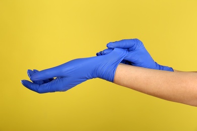 Woman putting on blue latex gloves against yellow background, closeup of hands