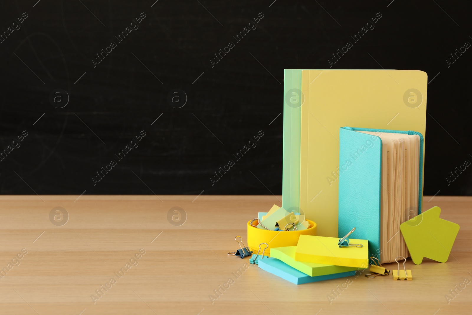 Photo of Different school stationery on wooden table near blackboard, space for text. Back to school