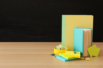 Different school stationery on wooden table near blackboard, space for text. Back to school