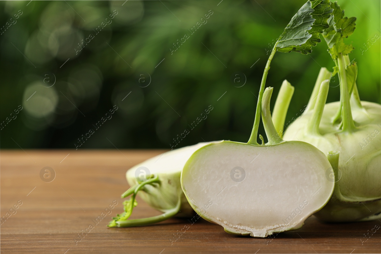 Photo of Whole and cut kohlrabi plants on wooden table. Space for text