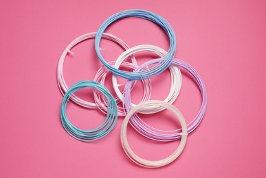 Photo of Colorful plastic filaments for 3D pen on pink background, flat lay