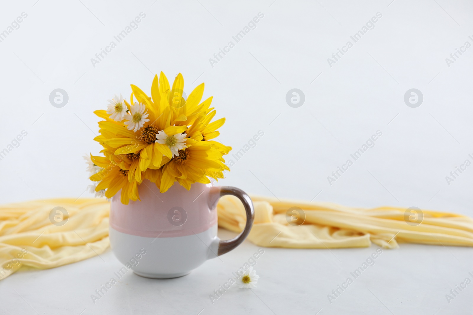 Photo of Cup with beautiful flowers and cloth on white table. Space for text