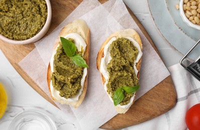 Photo of Tasty bruschettas with cream cheese, pesto sauce and fresh basil on white table, flat lay