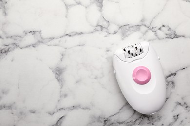 Modern epilator on white marble table, top view. Space for text