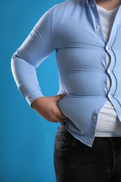 Photo of Overweight man in tight shirt on light blue background, closeup