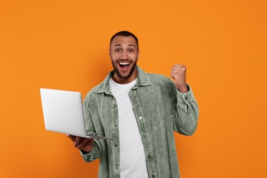 Photo of Happy young man with laptop on orange background