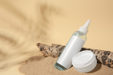 Cosmetic products and tree bark on sand against beige background. Space for text