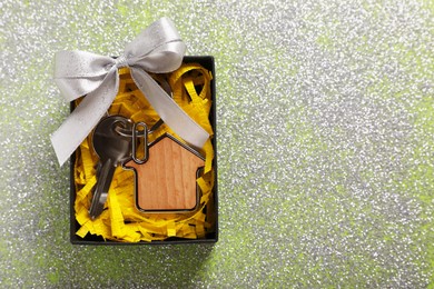 Key with trinket in shape of house, glitter and gift box on shiny surface, top view with space for text. Housewarming party
