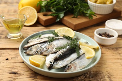 Photo of Fresh raw sprats, lemon and dill on wooden table, closeup