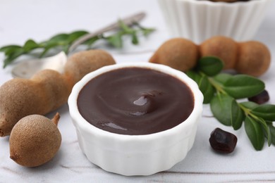 Photo of Bowl of tasty tamarind sauce and fresh pods on white textured table, closeup