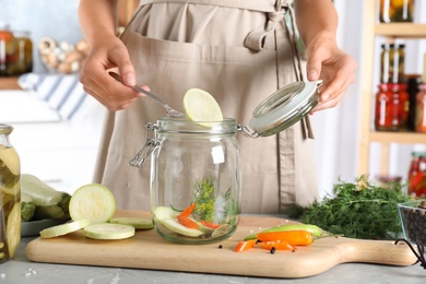 Photo of Woman putting slice of zucchini into jar at grey marble table indoors, closeup. Pickling vegetables