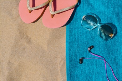 Photo of Soft blue beach towel with flip flops, sunglasses and earphones on sand, flat lay. Space for text