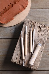 Clay and set of modeling tools on wooden table, flat lay