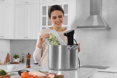 Photo of Woman putting vacuum packed broccoli into pot with sous vide cooker in kitchen. Thermal immersion circulator