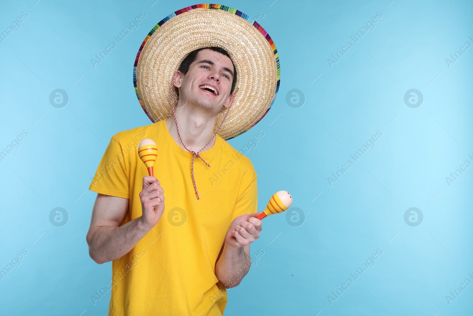 Photo of Young man in Mexican sombrero hat with maracas on light blue background. Space for text