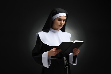 Photo of Young nun reading Bible on black background