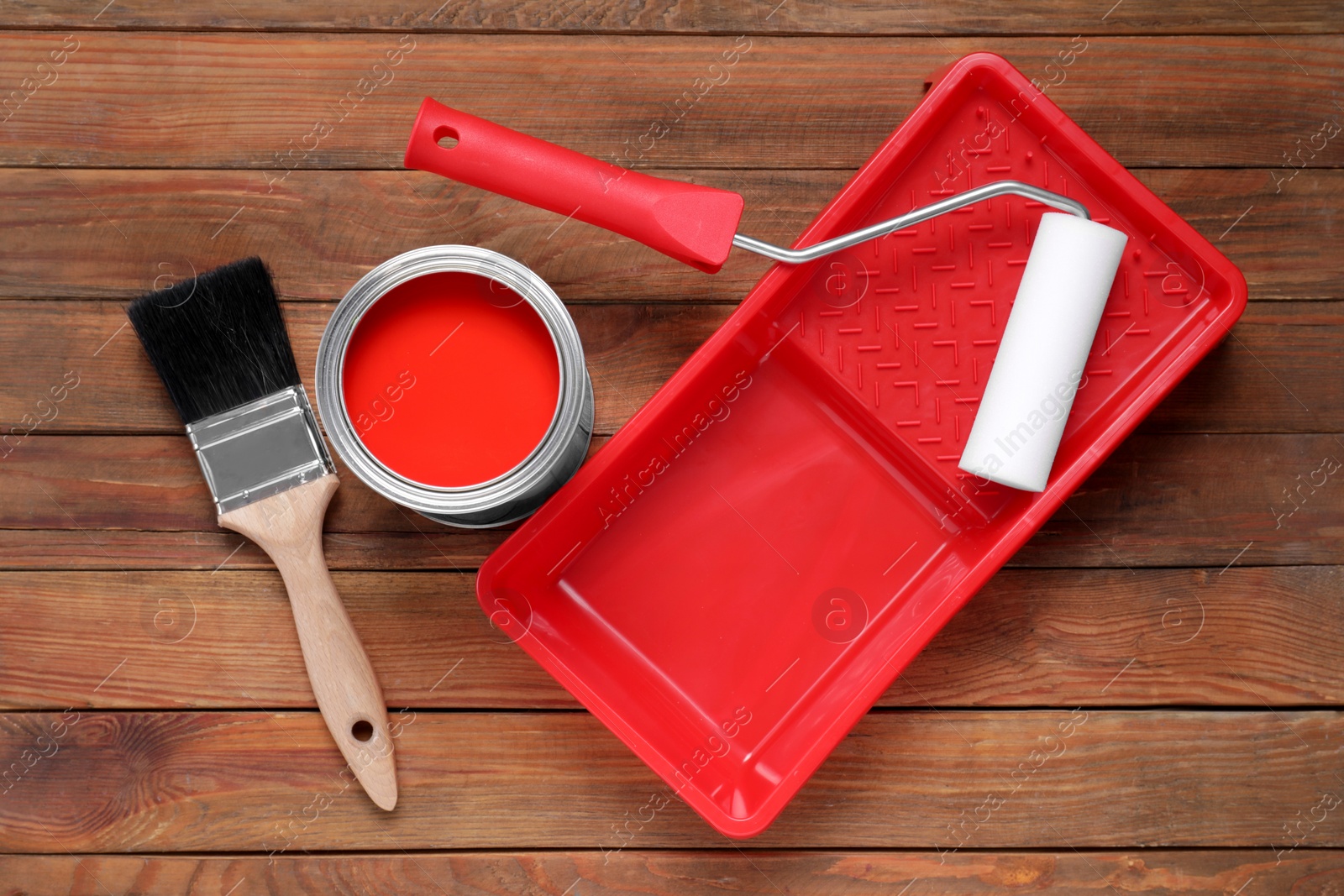 Photo of Can of red paint, brush, roller and tray on wooden table, flat lay