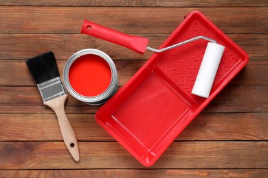 Can of red paint, brush, roller and tray on wooden table, flat lay