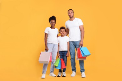 Family shopping. Happy parents and son with colorful bags on orange background