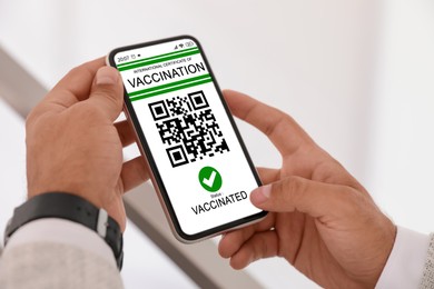 Man holding smartphone with international certificate of vaccination indoors, closeup