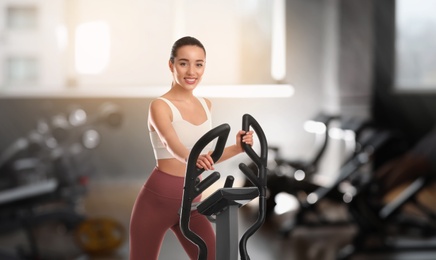 Image of Woman using modern elliptical machine in gym 