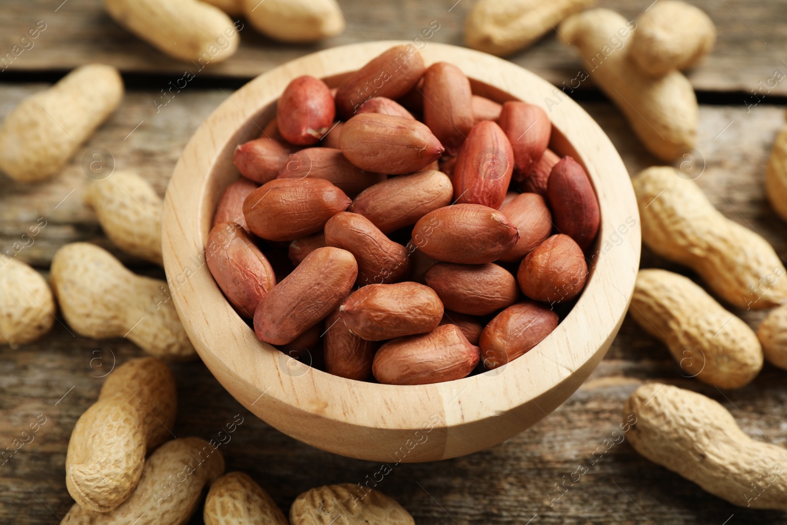 Photo of Fresh unpeeled peanuts in bowl on wooden table, closeup