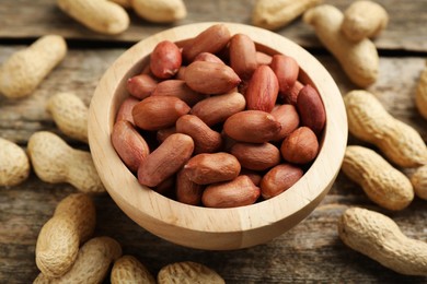 Fresh unpeeled peanuts in bowl on wooden table, closeup