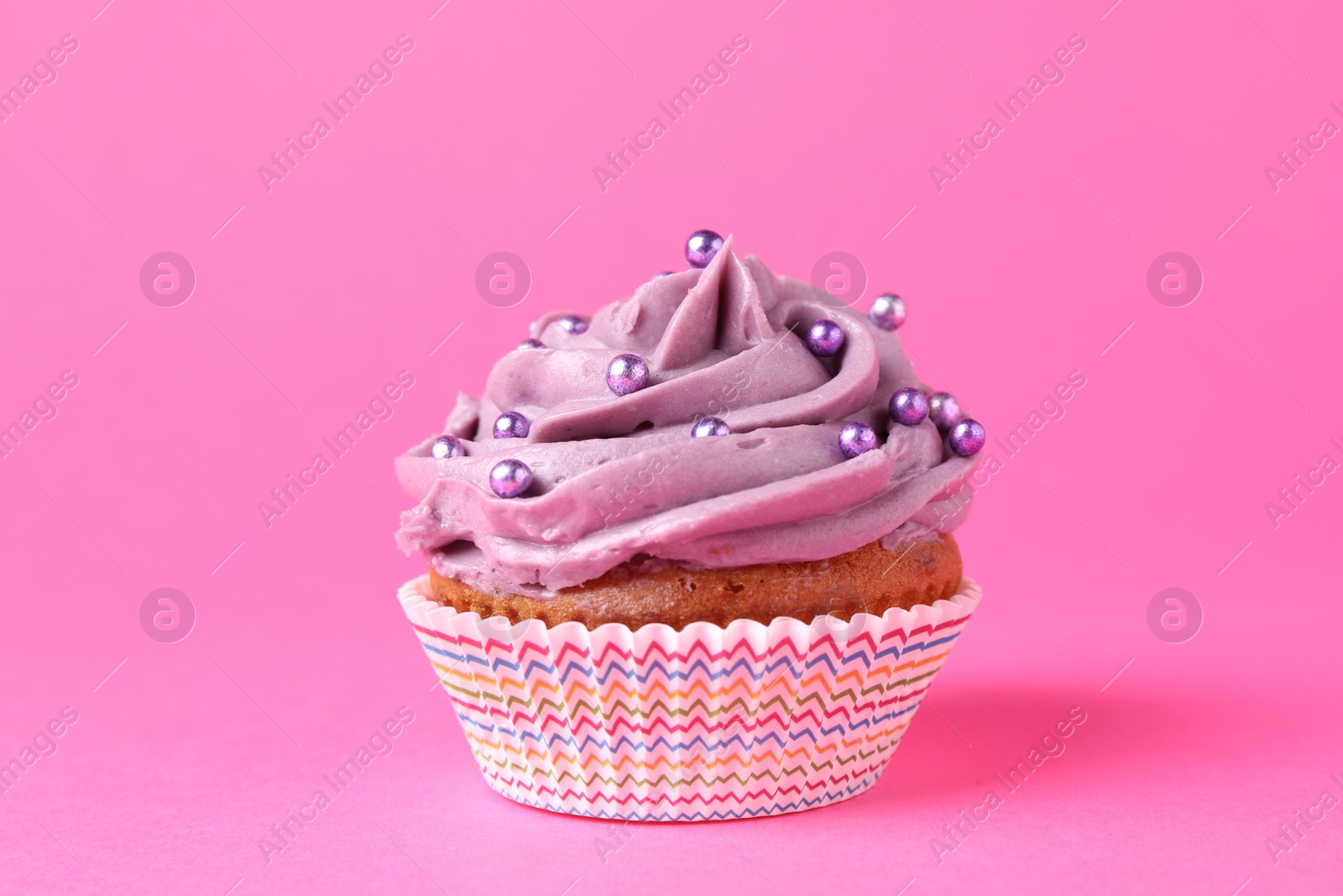 Photo of Delicious cupcake with bright cream and sprinkles on pink background