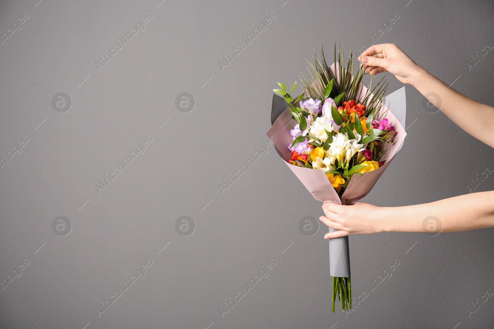 Photo of Woman with beautiful bouquet of freesia flowers on grey background