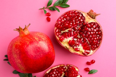 Photo of Fresh pomegranates and green leaves on pink background, flat lay