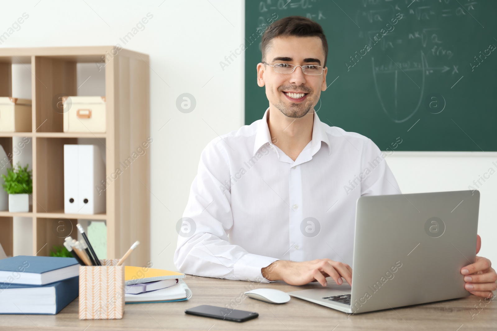 Photo of Young male teacher with laptop sitting at table in classroom