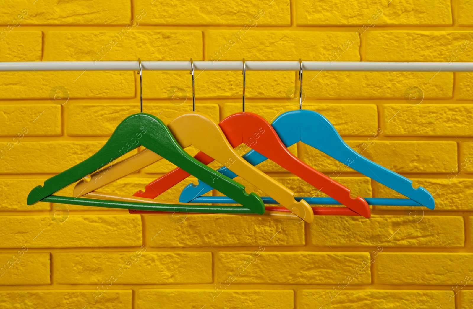 Photo of Wardrobe rack with many hangers near yellow brick wall