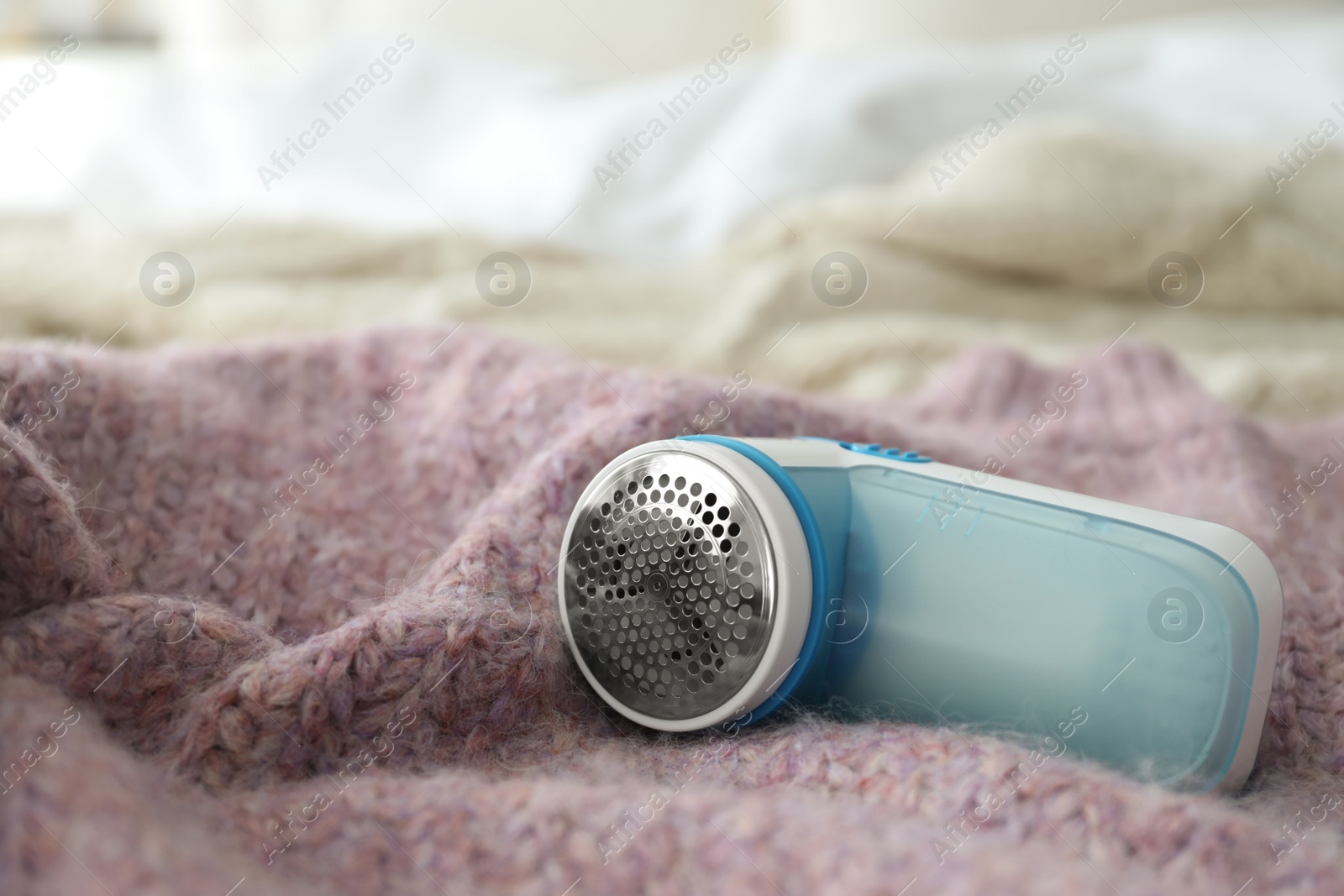 Photo of Modern fabric shaver on pink woolen sweater, closeup. Space for text