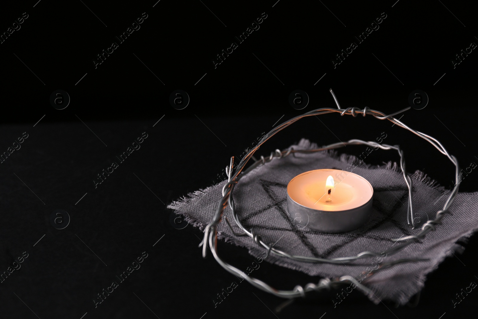 Photo of Fabric with star of David, barbed wire and burning candle on black background, space for text. Holocaust memory day