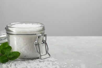 Photo of Natural sea salt in glass jar and mint on light grey marble table, space for text