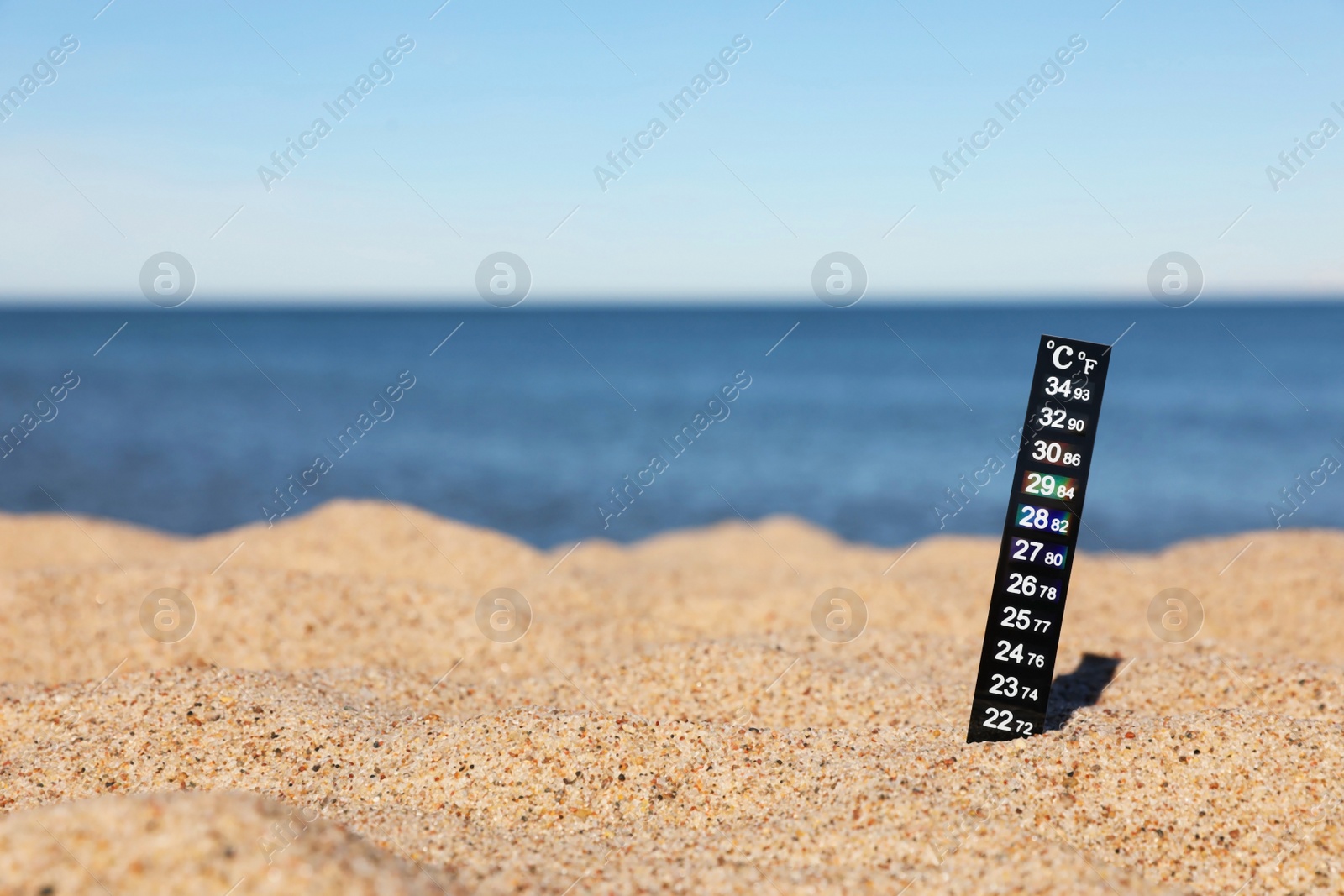 Photo of Weather thermometer in sand near sea, space for text