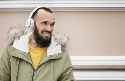 Photo of Mature man with headphones listening to music near light wall. Space for text