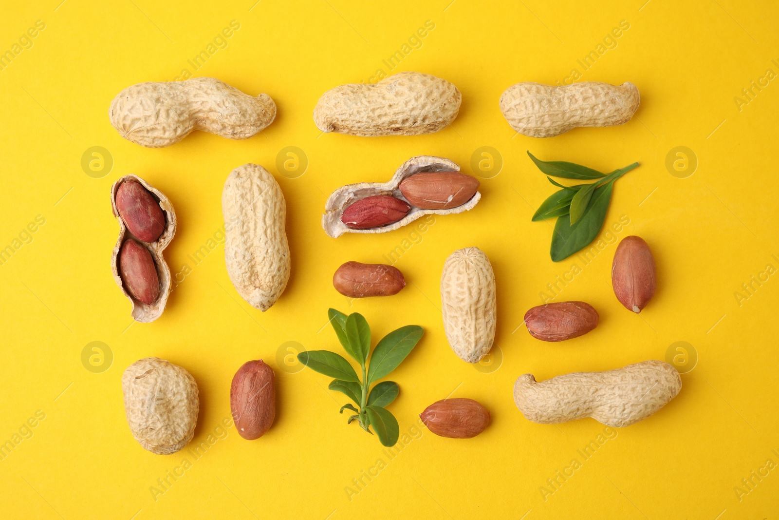 Photo of Fresh peanuts and leaves on yellow table, flat lay